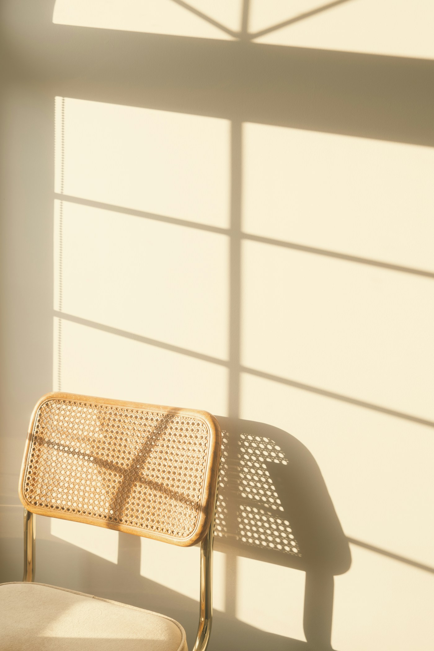 A pale cane chair against a warm wall crossed by afternoon window light
