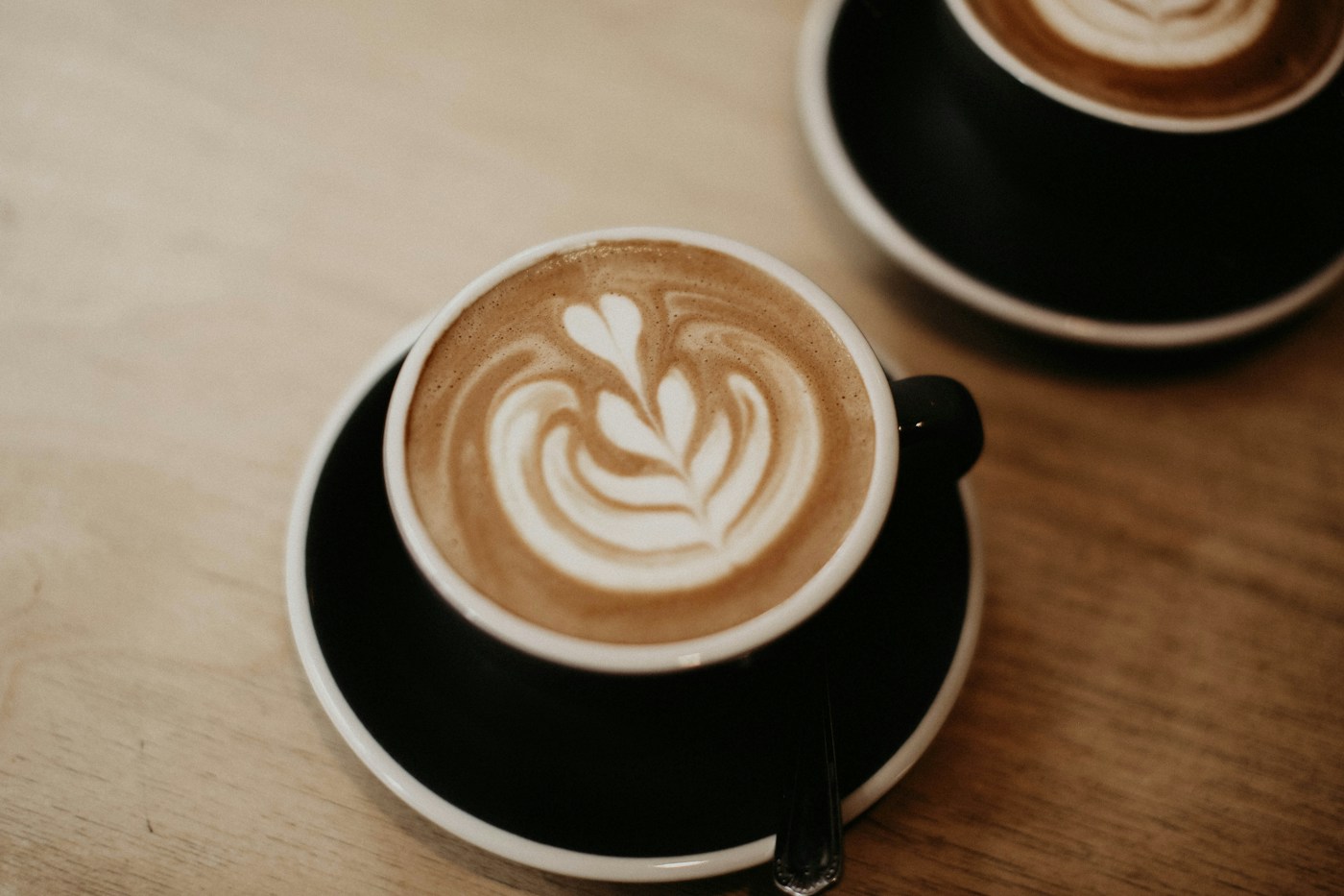 Two charcoal coffee cups on a pale wooden table
